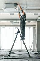Standing on, the, ladder. Repairman in uniform is in the unfinished building photo