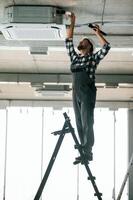 Standing, on the ladder. Repairman in uniform is in the unfinished building photo