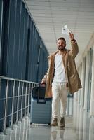 Running, late for flight, with tickets ,in hand. Young handsome man in the airport photo