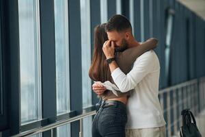 Man is crying, embracing,, farewell. Couple are in the airport hall together photo