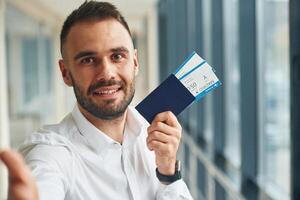Smiling, holding tickets. Young handsome man in the airport photo