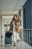 Running, late fo,r flight, with tickets in hand. Young handsome man in the airport photo