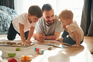 Lying down, ,,board game. Father is playing with two little boys on the floor with toys photo