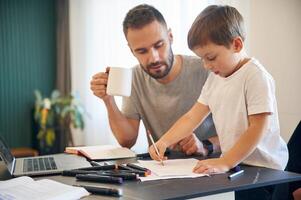 Doing homework.. Father ,and son are at home by the table photo
