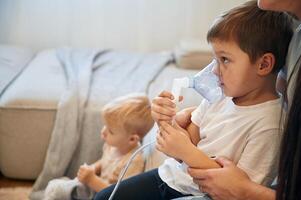 Boy is making, inhalation, with, nebulizer to reduce coughing. Mother with her little son is at home in domestic room photo