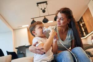 Inhalation with, nebulizer to reduce coughing. Mother with her little son is at home in domestic room photo
