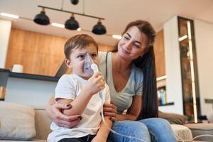 Inhalation, with nebulizer to reduce coughing. Mother with her little son is at home in domestic room photo