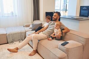 Smiling, positive, facial expression. Father with two baby boys is sitting at sofa photo