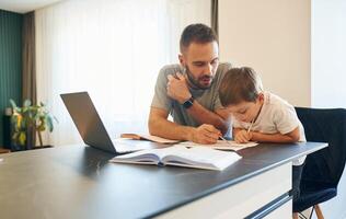 Writing ,,the homework. Father and son are at home by the table photo