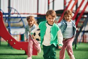 Boy, is in green clothes, with soccer ball. Kids are having fun on the playground photo