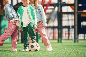 Boy is, in green clothes, with soccer ball. Kids are having fun on the playground photo