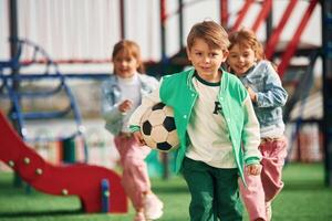Boy is in, green clothes, with soccer ball. Kids are having fun on the playground photo