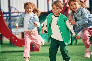 Boy is in green clothes,, with soccer ball. Kids are having fun on the playground photo
