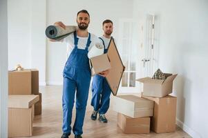 Mat and painting in hands. Two moving service employees in ,,a room photo