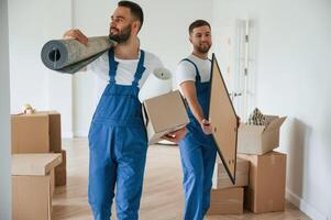 Mat and painting in hands. Two moving service employees in a ,room photo