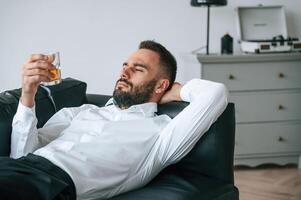 On the black sofa. Upset young man ,drinker alcoholic is indoors photo