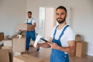 Writing in notepad, holding box.. Two moving service employees in a room photo