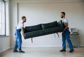 Sofa in hands. Two, moving ,service employees in a room photo