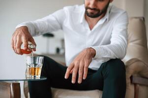 Pouring the, whiskey into the glass. Upset young man drinker alcoholic is indoors photo