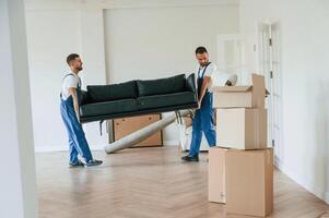 Holding heavy sofa. .Two ,moving service employees in a room photo