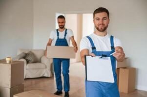 Sign in the documents.. Two moving service employees in a room photo