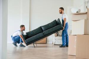 Holding heavy, sofa. Two moving service employees in a room photo