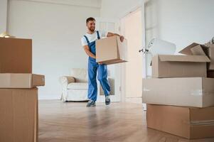 White shirt ,and blue uniform. With box in hands. Moving service employee in a room photo