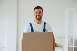 White shirt,, and blue uniform. With box in hands. Moving service employee in a room photo