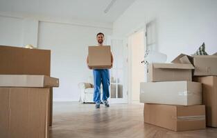 White,, shirt and blue uniform. With box in hands. Moving service employee in a room photo