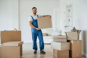 Full ,height photo, standing and holding big box. Moving service employee in a room photo