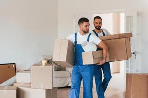 Front view, holding,, stuff. Two moving service employees in a room photo