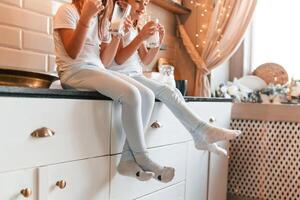 Close up view of two little girls that are drinking milk while sitting on the table on the kitchen photo