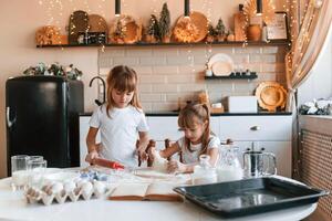 Working with dough. Two little, girls ,are preparing food on the kitchen with garlands photo