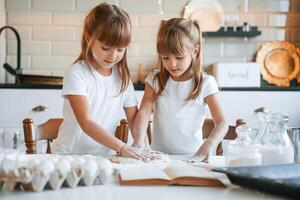 Flour ,and, eggs on the table. Two little girls are preparing food on the kitchen with garlands photo