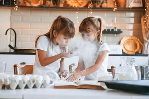 Using flour. ,Two, little girls are preparing food on the kitchen with garlands photo