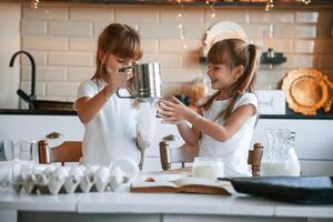 Using flour., Two little girls are preparing food on the kitchen with garlands photo