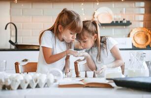 Using, flour. Two, little girls are preparing food on the kitchen with garlands photo