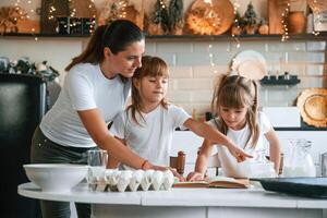 Learning how to prepare food... Mother with her little two daughters is on the kitchen with garlands photo