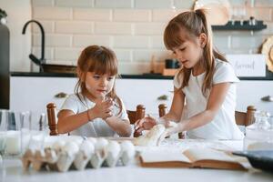 Flour and, eggs on the table. Two little girls are preparing food on the kitchen with garlands photo
