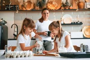 Learning how to prepare food. Mother, with her little two daughters is on the kitchen with garlands photo