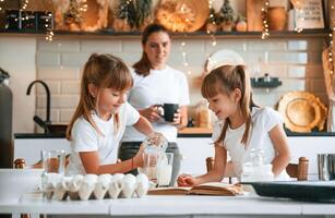 Learning how to, prepare food. Mother with her little two daughters is on the kitchen with garlands photo