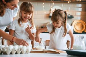 Using quality products. Mother ,,with her little two daughters is preparing food on the kitchen with garlands together photo