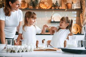 Learning ,how ,to prepare food. Mother with her little two daughters is on the kitchen with garlands photo