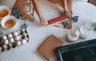 Close up top view of kid's hands that knead the dough on the table with eggs photo