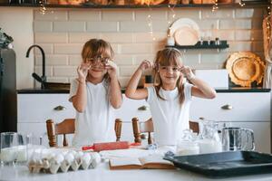 Holding forms for the best rolled sugar cookies. Two little girls are preparing food on the kitchen with garlands photo