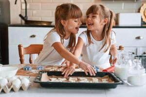 Smiling, playful, mood. Two,, little girls are preparing food on the kitchen with garlands photo
