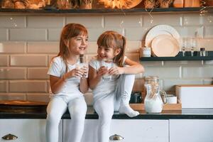 Having, fun.. Happy two little girls are drinking milk while sitting on the table on the kitchen photo