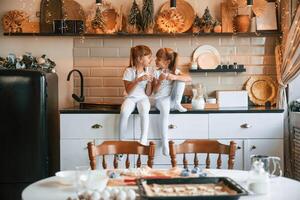 Having, fun. Happy two little girls are drinking milk while sitting on the table on the kitchen photo