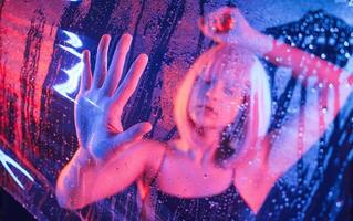 Hands are,, on the surface. Stylish woman ,with white hair is behind wet transparent plastic sheet photo