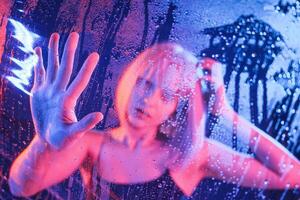 Trapped ,inside, with hands ,on surface. Stylish woman with white hair is behind wet transparent plastic sheet photo